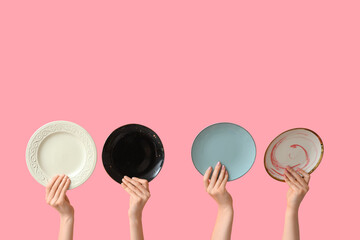 Hands holding empty plates on pink background