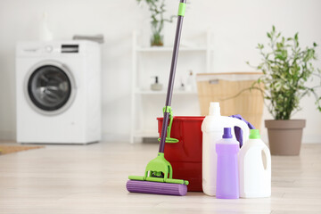 Mop with bucket and different cleaning supplies on floor at home