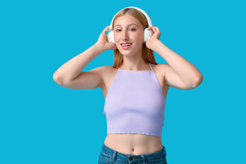 Beautiful young happy woman in stylish summer outfit and headphones on blue background
