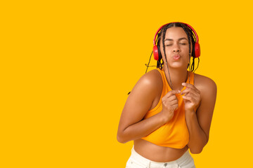 Emotional African-American woman listening to music on yellow background