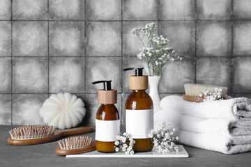 Composition with bottles of shampoo, flowers and towels on table near grey grunge tile wall