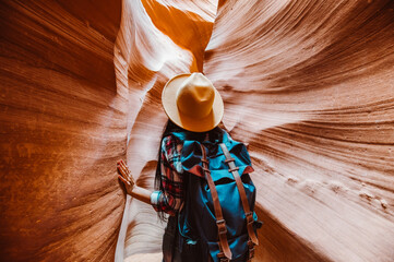 Backpacker Standing Inside a Narrow Antelope Canyon with Sunlit Orange Sandstone Walls and a Serene Sky View in Arizona, USA © Victoria Nefedova