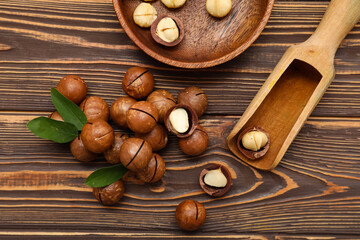 Bowl and scoop with tasty macadamia nuts on wooden background