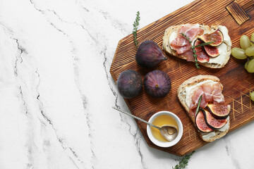 Wooden board of delicious fig bruschetta with prosciutto and ricotta cheese on white background