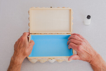 Senior man placing blue felt inside a handcrafted seashell jewelry box, top view.