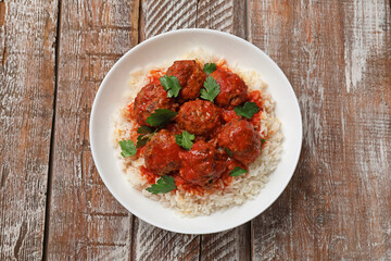 Tasty meatballs with sauce and rice on wooden table, top view