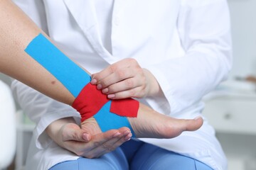 Doctor applying kinesio tapes to patient's foot in hospital, closeup