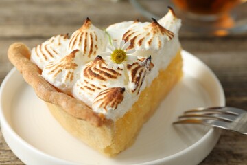 Piece of delicious pie with browned meringue and fork on wooden table, closeup