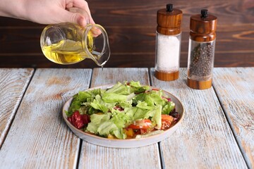 Woman pouring oil onto tasty salad at color wooden table, closeup