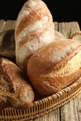Different loaves of fresh bread in basket on wooden table, closeup
