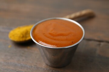Tasty curry sauce in metal dish and powder on wooden table, closeup
