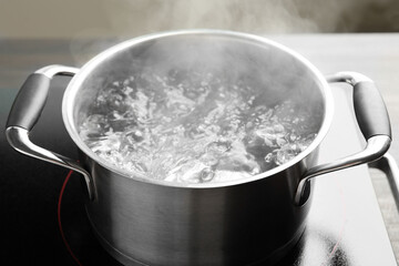 Cooking pot with boiling water and stove on table against grey background, closeup