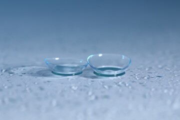 Pair of contact lenses and water drops on color mirror surface, closeup