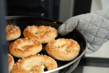 Woman taking baking dish with fresh pretzels out of oven, closeup
