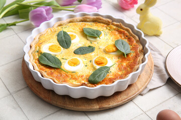 Delicious Easter egg tart with spinach leaves and tulip flowers on white tile background, closeup
