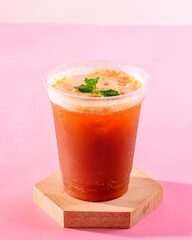 A glass of iced tea with a green leaf on top. The drink is served in a plastic cup