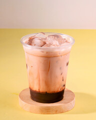 A cup of chocolate drink with ice in it. The drink is served in a plastic cup. The cup is placed on a wooden coaster