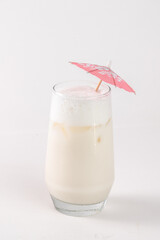 A tall glass filled with white milk is topped with a pink umbrella. The umbrella is made of paper and has a pink and white design. The glass is almost full
