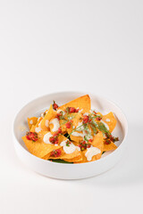 A white bowl filled with yellow nachos topped with a creamy sauce. The bowl is placed on a white background, creating a simple and appetizing presentation