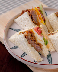 A plate of sandwiches with a variety of fillings, including ham, cheese, and avocado. The sandwiches are cut into triangles and arranged on a white plate