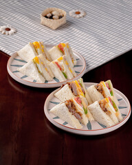 Two plates of sandwiches on a table. The sandwiches are cut into triangles and are on white plates
