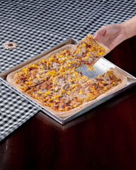 A person is holding a slice of pizza with corn on it. The pizza is cut into four pieces