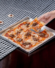 A person is holding a slice of pizza with a spatula. The pizza is topped with onions and meat