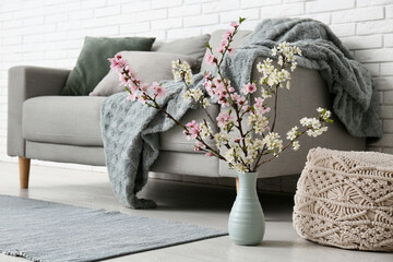 Vase of blooming branches on floor near sofa in living room
