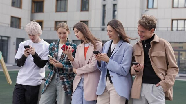 A group of international young friends laughs together, gathered in a circle as they scroll through their phones. With smiles on their faces, they watch funny videos online, caught up in the