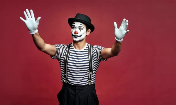 Male mime in black hat and stripe shirt on red background, gesturing with hands