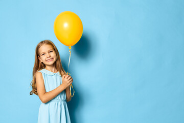 Fototapeta premium Little girl holding a yellow balloon against a vibrant blue background with ample copy space for text