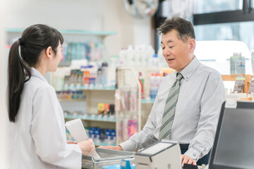 薬局,ドラックストアのレジで処方箋の説明を受けるシニア男性

