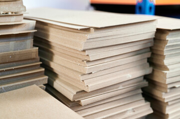 Thick stacks of paperboard ready for cardboard box manufacturing in a bustling workshop environment