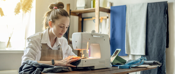 A female tailor is working on a sewing machine stitching fabric in sunny room. Home sewing...