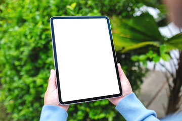 Mockup image of a woman holding digital tablet with blank white desktop screen in the nature outdoors