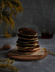Pancakes in rows stacked close-up with honey and mimosa on a gray background