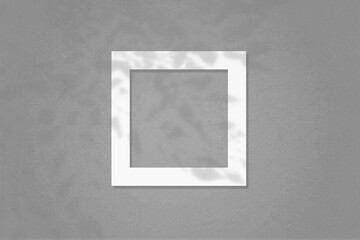Natural light casts shadows from the wildflowers on square frame of white textured paper lying on a gray facture background. Mock up with an overlay of plant shadows