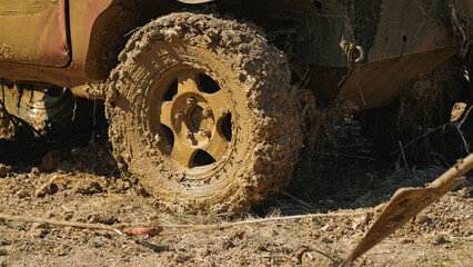 A close-up of a mud-covered SUV tire. The whole vehicle and suspension elements in sticky mud and grass. Extreme off-road races.