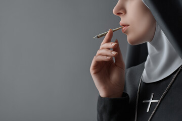 Cropped view of nun smoking marijuana joint isolated on grey
