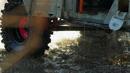 The solid tire of the car with the red rim was partially submerged in the muddy water, droplets flying around. Washing the off-road vehicle after the competition.