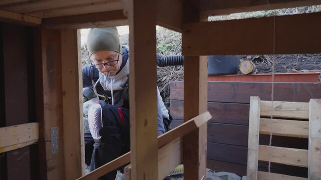 Man working on wooden wall repair outdoors during the old barn renovation. He uses hand tools and lumber to improve the structure. DIY, construction, and home maintenance.