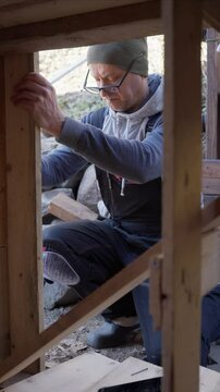 Man working on wooden wall repair outdoors during the old barn renovation. He uses hand tools and lumber to improve the structure. DIY, construction, and home maintenance.