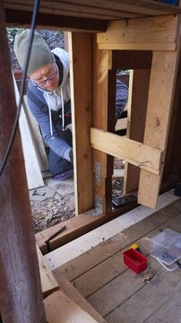 Man working on wooden wall repair outdoors during the old barn renovation. He uses hand tools and lumber to improve the structure. DIY, construction, and home maintenance.