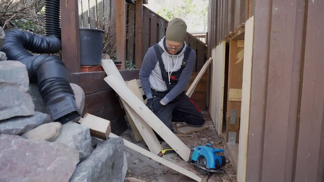 Man working on wooden wall repair outdoors during the old barn renovation. He uses hand tools and lumber to improve the structure. DIY, construction, and home maintenance.