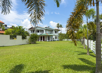 A large house with a lush green lawn and palm trees in the background