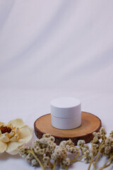 A minimalist and serene flat lay composition featuring a white, round cosmetic jar or container...
