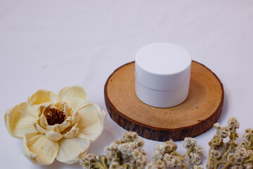 A minimalist and serene flat lay composition featuring a white, round cosmetic jar or container resting on a natural, circular wooden.