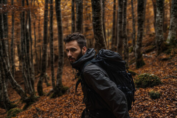 The image shows a man hiking in a forest during autumn, wearing a backpack and a jacket, surrounded by trees with brown leaves on the ground