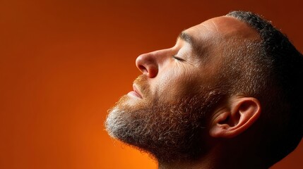 Obraz premium Man in profile enjoying a moment of serenity against an orange backdrop