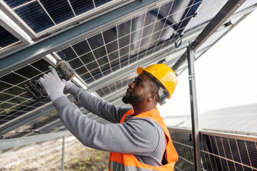Side view of multicultural worker standing under solar panels at solar farm and fixing panels.